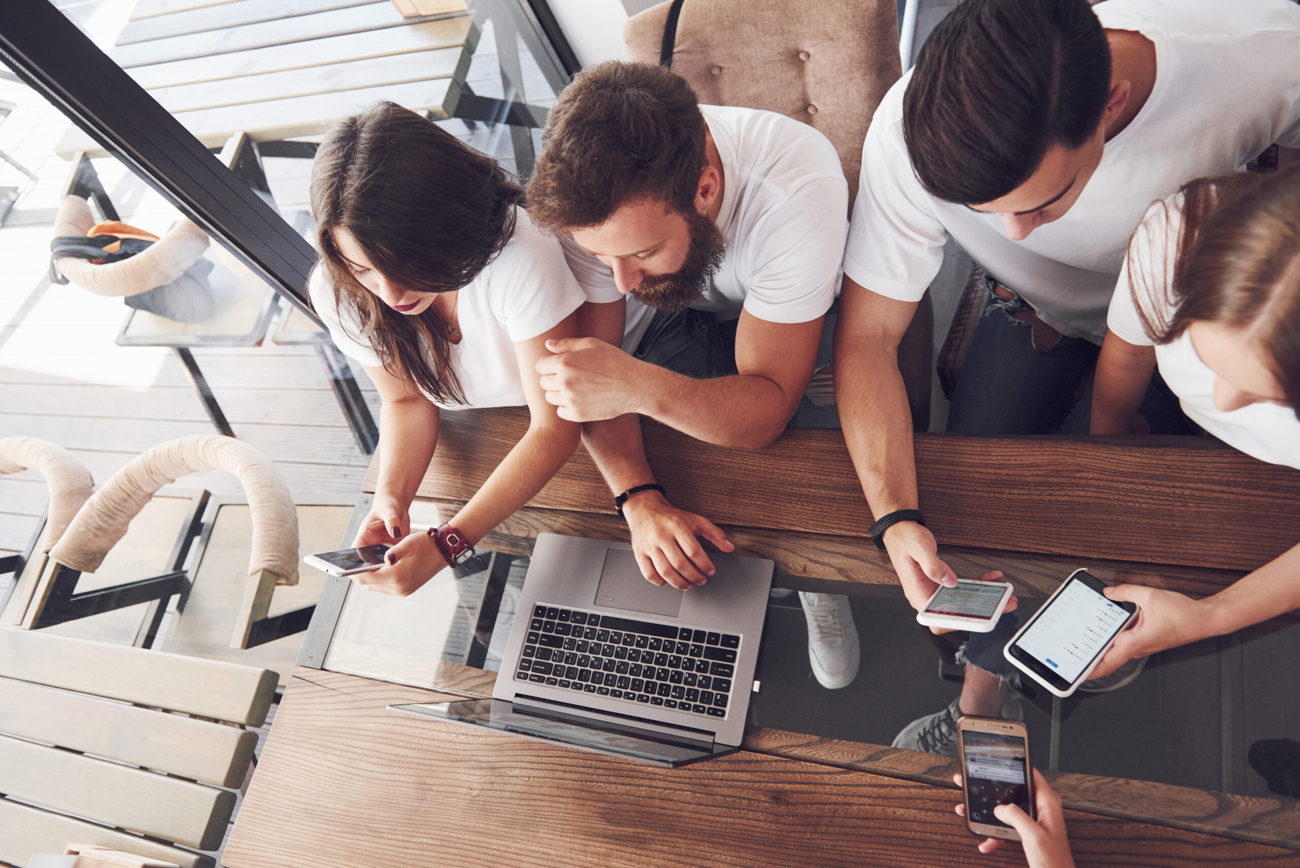 A group of young people with gadgets and a laptop arrange a brainstorm and communicate with each other. The concept of developing a young business